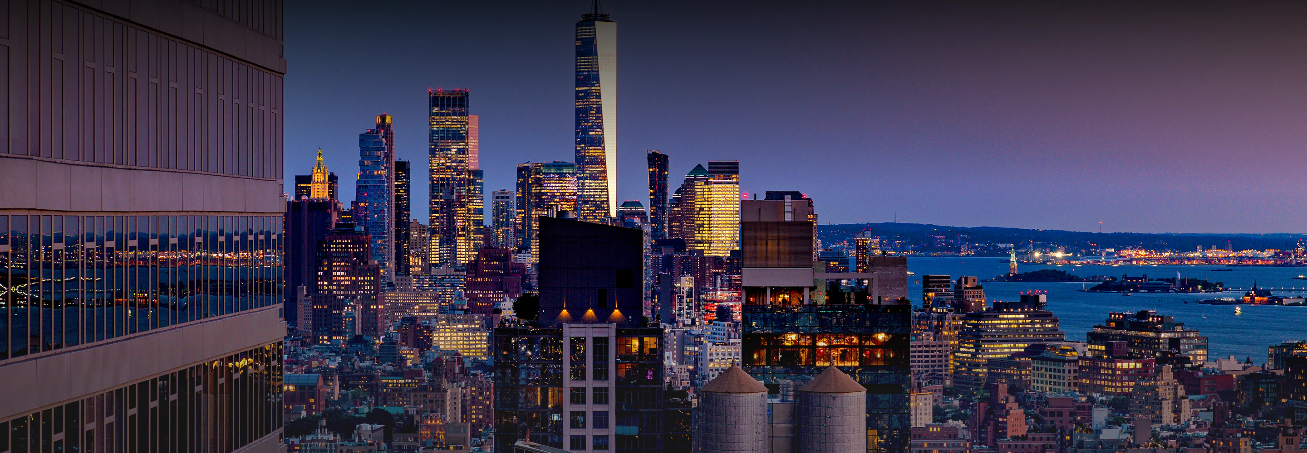 A panoramic view of a city skyline at New York, with buildings silhouetted against a colorful twilight sky.